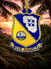 A decorative hanging ornament shaped like a military-style crest with the words 'BLUE ANGELS' on a yellow banner, shown against a tropical sunset and palm tree background.